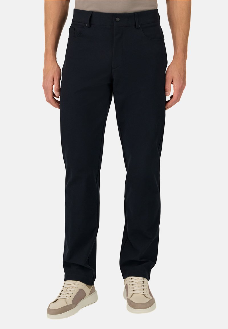 Pantalones azul marino de tela suave, con un corte clásico, dos bolsillos laterales y cierre frontal con botón. Combinados con zapatillas ligeras.