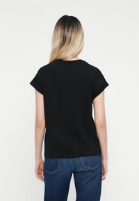 Tricou negru din bumbac cu mâneci scurte rulate, decolteu rotund și croială relaxată, asortat cu blugi denim albaștri.