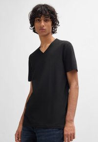 Tricou negru cu decolteu în V, cu mâneci scurte �și o textură simplă și netedă. Fabricat dintr-un material moale, asociat cu blugi albaștri.