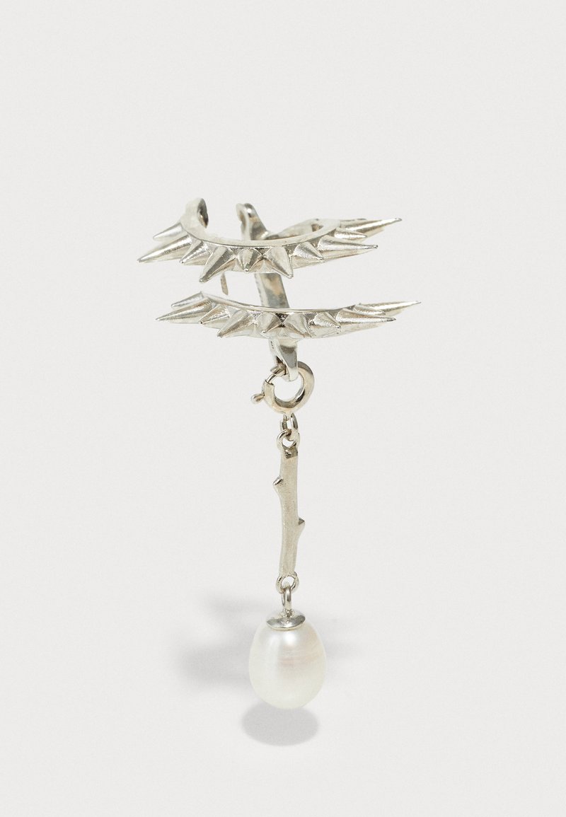 Srebrny nausznik z ostrymi kolcami i wiszącym detalem gałęzi, z białą perłą na końcu. Gładka tekstura, metaliczny wykończenie.