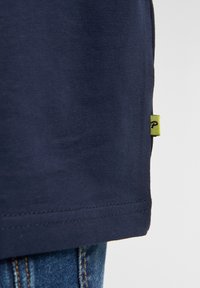 Navyblauwe katoenen T-shirt met een rechte zoom, voorzien van een klein limoengroen label aan de zijkant. Gladde textuur en eenvoudig ontwerp.