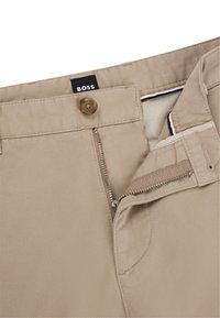 Beige színű pamut nadrág, elöl cipzárral és gombos záródással, belső kontrasztos csíkos részletekkel. Látható címke: 'BOSS.' Közepes súlyú anyag.