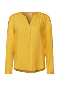 Blusa gialla a maniche lunghe con scollo a V, chiusura a bottoni, leggere arricciature sulle spalle e orlo curvo.