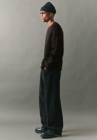 Tamna flis dukserica, rebraste crne kordura hlače i crne gležnjače. Dodaci uključuju pleteni beani i naočale. Bočni profil.