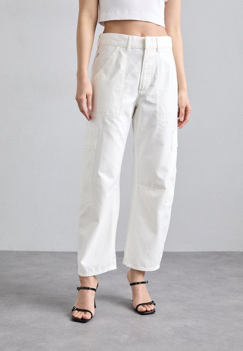 Pantalones cargo blancos de pierna ancha, con bolsillos frontales y una textura de algodón suave. Combinados con tacones negros de tiras.