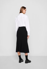 Cămașă albă cu nasturi și fustă midi din tricot cu nervuri negre. Șosete negre până la glezne și pantofi negri lustruiți. Design minimalist, culori solide.