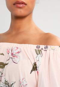 Top off-the-shoulder in tessuto rosa chiaro con stampa floreale. Presenta un collo elastico, una consistenza morbida e dettagli delicati.