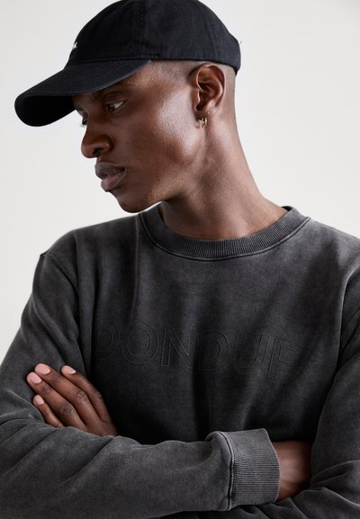 Felpa grigio scuro con lettering testurizzato "PONDUP", scollatura rotonda e polsini a costine. Abbinata a un cappellino da baseball nero, mostrata di profilo.