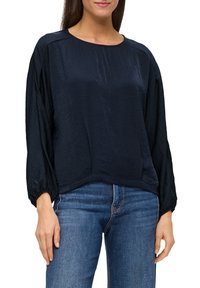 Navyblaue, langärmlige Seidenbluse mit rundem Ausschnitt, lässiger Passform und elastischen Bündchen. Kombiniert mit blauen Jeans.