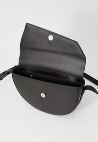 Borsa a tracolla in pelle nera con forma semicircolare, chiusura a scatto e un unico scomparto interno con tasca zip.