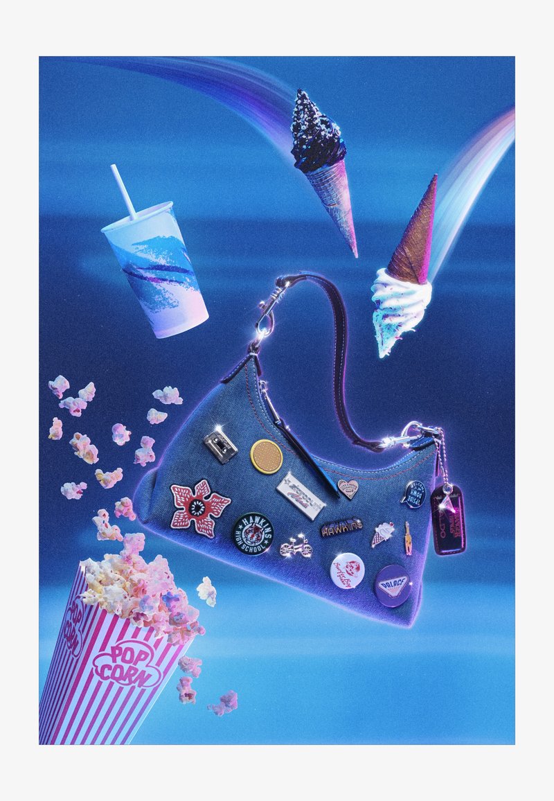 Denim handtas met pins drijft tussen popcorn, een frisdrankbeker en drie ijsjes tegen een blauwe achtergrond met lichtstralen.