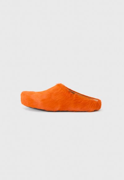 Oranges Hausschuhe aus Fell mit offenem Rücken, featuring einer glatten, abgerundeten Zehenpartie und weicher Textur, ruhend auf einer flachen schwarzen Sohle.