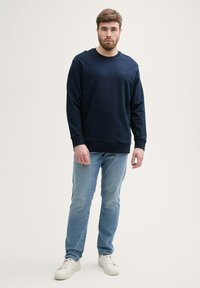 Marineblaues Sweatshirt mit langen Ärmeln und Rundhalsausschnitt, kombiniert mit hellblauen Jeans und weißen Turnschuhen. Glattes Material, bequeme Passform.