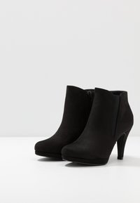 Bottes de cheville en suède noir avec des pointes pointues, une fermeture éclair sur le côté et de hauts talons aiguille. Texture lisse avec une couleur unie, accents de design minimaux.