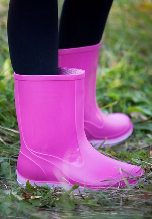 Bottes de pluie en caoutchouc rose avec une surface lisse et brillante, dotées d'un haut arrondi et d'une semelle blanche, posées sur une pelouse verte.