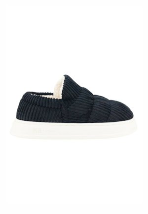 Zapato negro de pana tipo slip-on con un interior de crema suave, que presenta una suela blanca gruesa y un patrón texturizado en la parte superior.