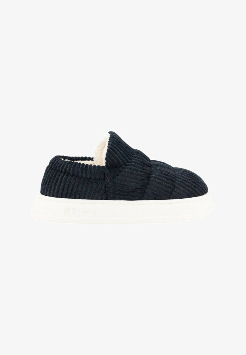 Zapato negro de pana tipo slip-on con un interior de crema suave, que presenta una suela blanca gruesa y un patrón texturizado en la parte superior.