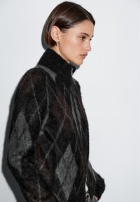 Sweter w czarno-szary wzór arlekin z wysokim kołnierzem, teksturowanej dzianiny i zamkiem błyskawicznym. Charakteryzuje się dopasowanym fasonem i miękkim wykończeniem.