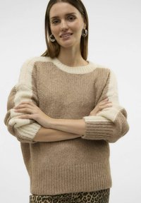 Pull en tricot bicolore beige et crème avec des poignets et un ourlet côtelés, présentant une coupe décontractée et un fil texturé.