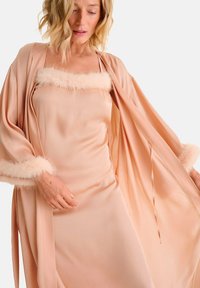 Robe en satin pêche avec un doux bord en fausse fourrure aux poignets et au col ; design fluide avec une ouverture à l'avant et des bretelles délicates pour un ajustement décontracté.