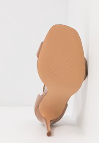 Chaussure à talon haut pour femme avec semelle beige, talon étroit et dessus en cuir marron clair, photographiée de côté contre un fond blanc.