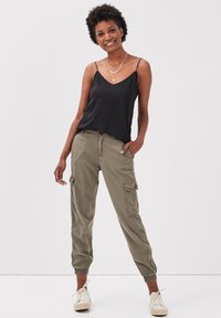 Top noir sans manches associé à un pantalon cargo vert olive avec des chevilles fuselées et des poches latérales. Modèle portant des baskets crème.