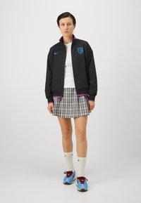 Black zip-up jacket with purple accents and England crest, white t-shirt, plaid pleated gray skirt, and blue athletic shoes with red laces.