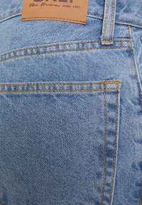 Light blue denim jeans feature a leather label with embossed text and yellow stitching along the pockets and seams.