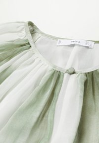Blusa plissettata verde e bianca con scollo rotondo, caratterizzata da un piccolo dettaglio con bottone al colletto e una texture di stoffa trasparente.