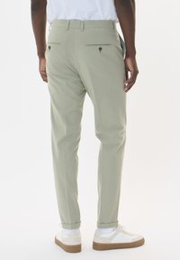 Light green tailored pants with a straight fit, buttoned back pockets, and cuffs rolled up. Paired with white and tan sneakers.
