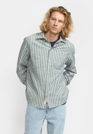 Gestreiftes Hemd mit Knopfverschluss aus blau-beigem Stoff, ausgestattet mit einer Brusttasche, lässigem Schnitt und langen Ärmeln. Trägt dazu hellblaue Jeans.