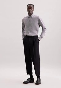 Tenue pour homme comprenant une chemise à boutons gris clair et un pantalon plissé noir. La chemise a un col classique, et les chaussures sont en cuir noir.