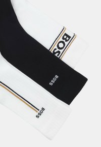 Drei Paar gerippte Socken: ein schwarzes mit weißem "BOSS"-Logo, ein weißes mit goldenen und schwarzen Streifen und Logo, aus weichem Baumwollmischgewebe.