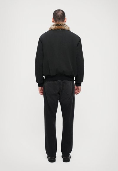 Svart bomberjacka med pälskrage, i kombination med mörka denimjeans. Tyget är mjukt, med avslappnad passform och ribbade muddar.