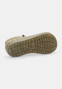 Talpă de sneaker bej cu suprafață din cauciuc texturat, având un model în grilă și mici resturi. Vârf rotunjit și detalii cu cusături vizibile.