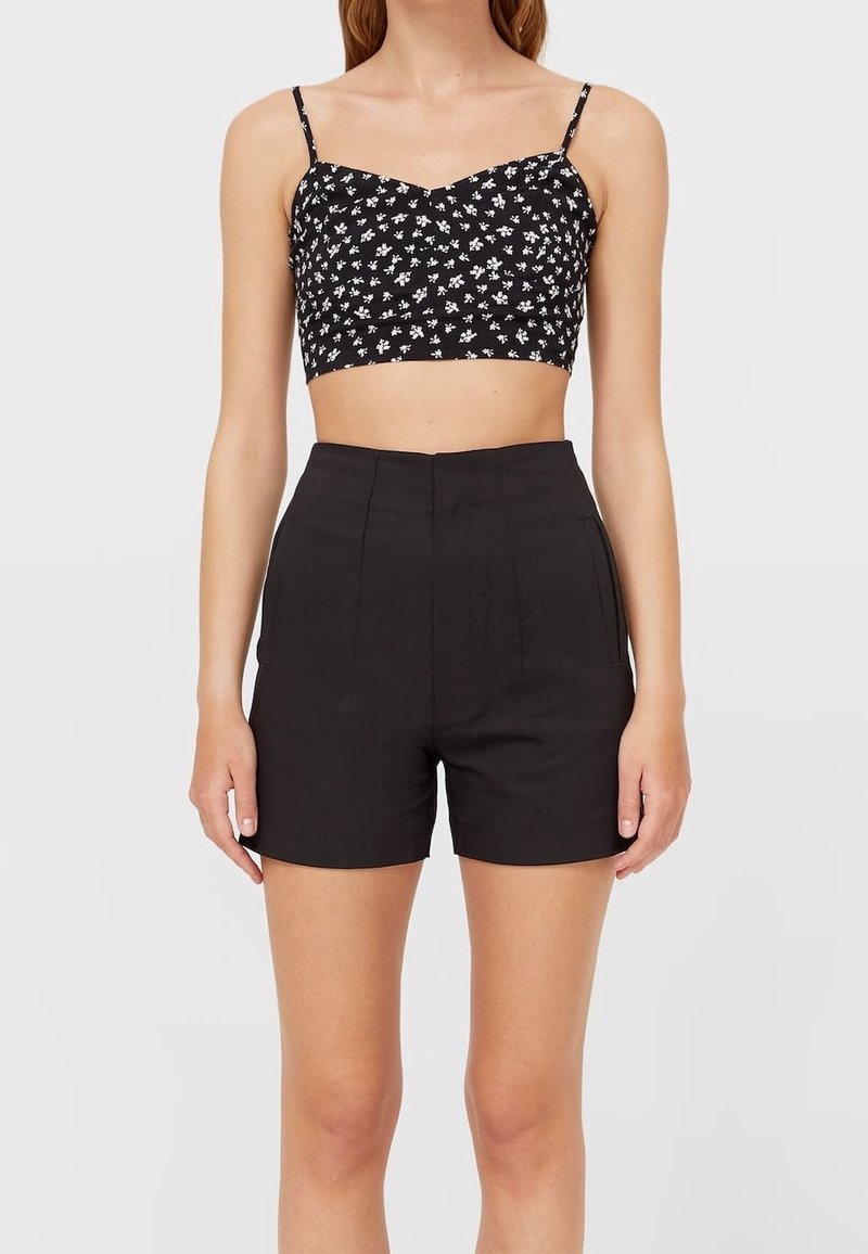 Zwart cropped top met wit bloemenprint en spaghetti bandjes, gecombineerd met hoog getailleerde zwarte shorts met voorplooien en zakken.