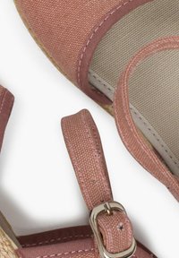 Sandal espadrille de lona rosa con una tira de tela. Cuenta con un hebilla, suela texturizada y un forro interior de color claro.