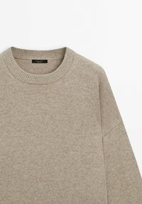 Pull en maille beige à col rond, avec col en côte et manches longues, présenté sur un fond blanc uni.