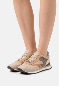 Beige and tan sneakers with suede and leather materials, featuring a lace-up design, contrasting accents, and a rubber sole.
