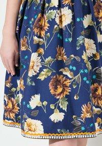 Kukka-aiheinen mekko, jossa on tumma sininen kangas, jossa on keltaisia ja ruskeita kukkia, turkooseja helmiä ja koristeellinen trimmi, jossa on oranssia sahalaitakuviota.