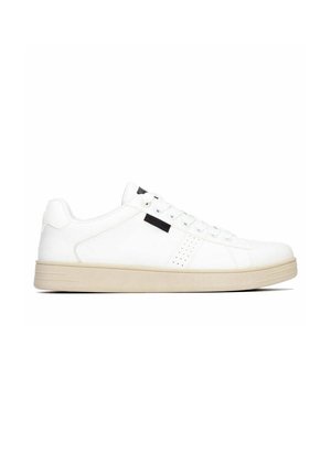 Zapatilla blanca de caña baja con suela beige, cierre de cordones, pequeña etiqueta negra cerca de los cordones y detalle perforado en el lateral.