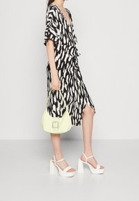 Vestido de estampado en blanco y negro con mangas cortas, combinado con sandalias de plataforma blancas y un bolso verde claro con una hebilla decorativa.