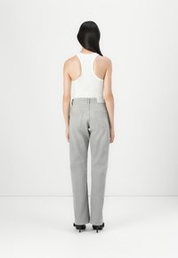 Un débardeur blanc à côtes associé à un jean taille haute gris clair. Le jean a une coupe droite et des détails subtils sur les poches arrière.