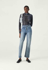 Top de manga larga con estampado de serpiente negra y tira de hombro gris, combinado con jeans rectos de color azul claro con cierre de cremallera y botón.