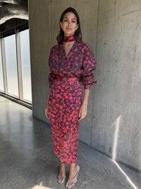 Rochie cu model floral roșu, cu mâneci lungi, cu button-up în față și o siluetă ajustată. Combinată cu sandale cu toc deschis și curele.