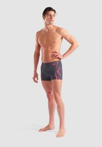 Męskie kąpielówki w ciemnoszarym kolorze z różowym geometrycznym wzorem. Wykonane z gładkiego, elastycznego materiału. Dopasowany fason z krojem sięgającym do połowy uda.
