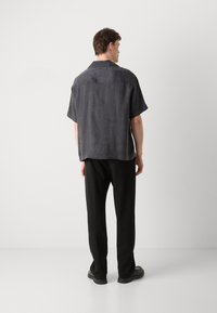 Camisa de manga corta con cuello en tejido gris oscuro, con una textura suave y costuras mínimas, combinada con pantalones negros y zapatos planos.