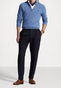 Ljusblå zip-up tröja, vit skjorta under, randiga marinblå byxor och bruna loafers. Inkluderar en mönstrad scarf och klocka.