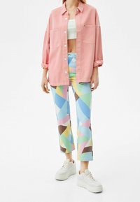 Rosa overskjorta med knäppningar, parat med färgglada mönstrade byxor i geometriska former. Vita sneakers fulländar stilen.