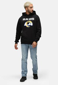 Sudadera negra con capucha y texto blanco "RAMS" junto con un logo azul y amarillo de "LA". Combinada con jeans de color azul claro y zapatos negros.